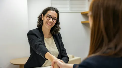 Two people greeting each other across a desk at an interview
